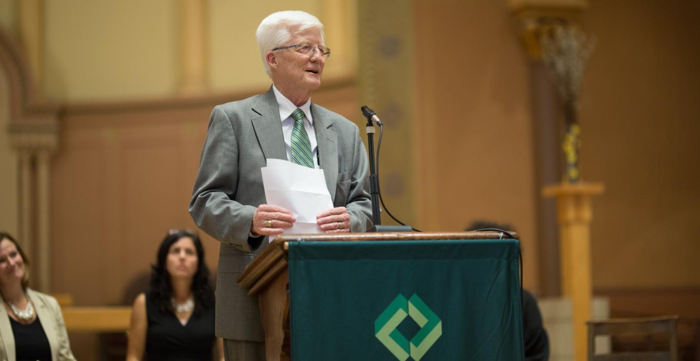 Interim President Hansen stands at a podium speaking into a microphone