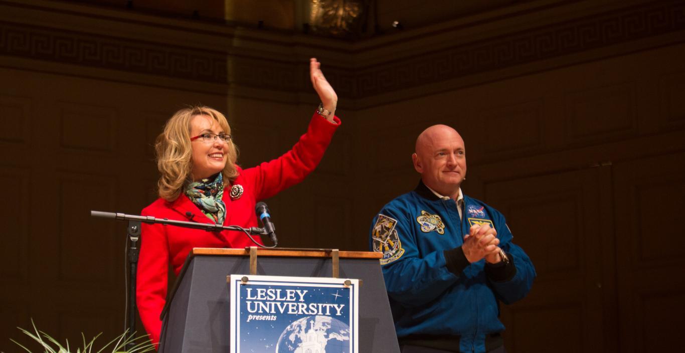 Gabby Giffords waves and Mark Kelly clasps his hands on stage.