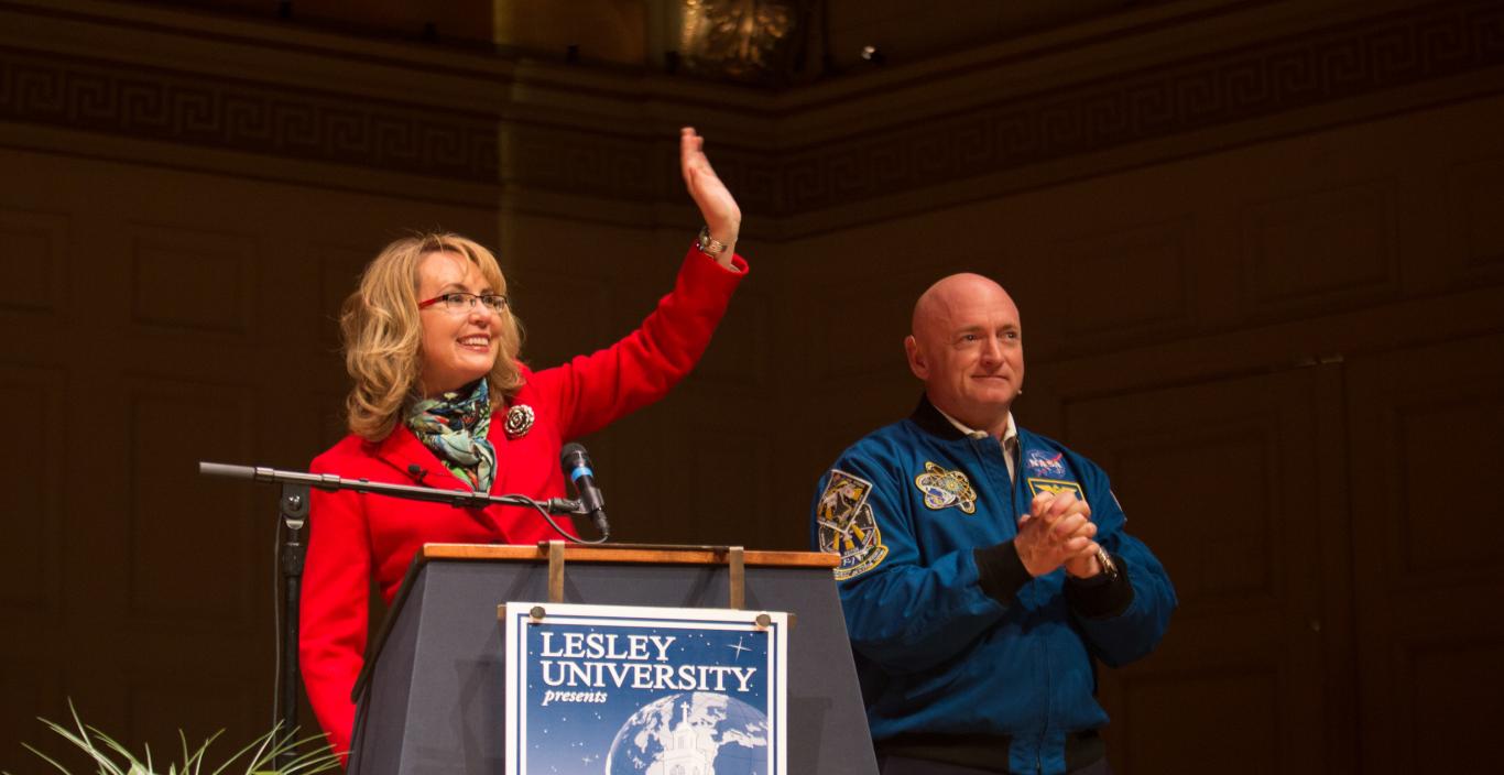 Gabby Giffords waves and Mark Kelly clasps his hands on stage.