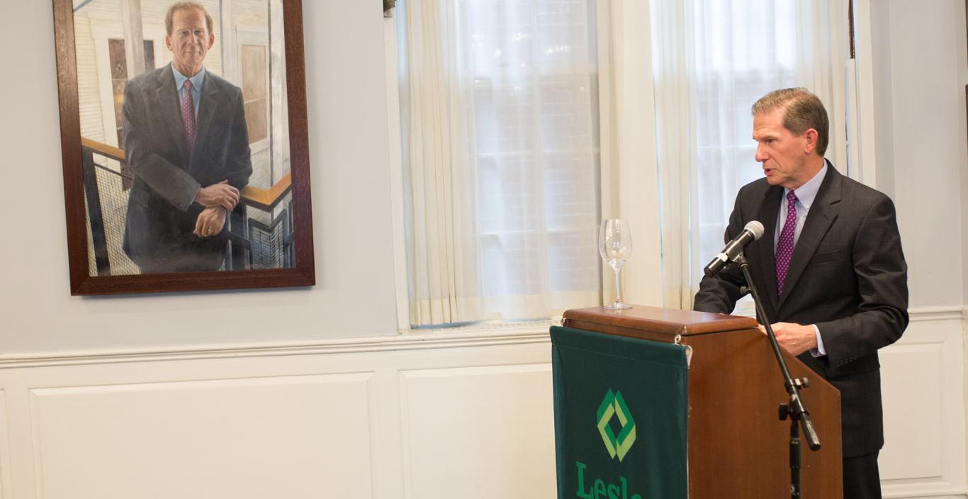 Joe Moore speaks at a podium in Alumni Hall in the foreground of his portrait