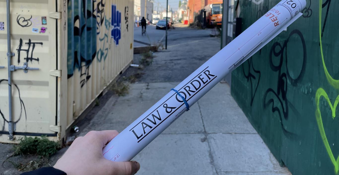 Outside, NYC, hand holding a rolled up paper printed with "Law & Order"
