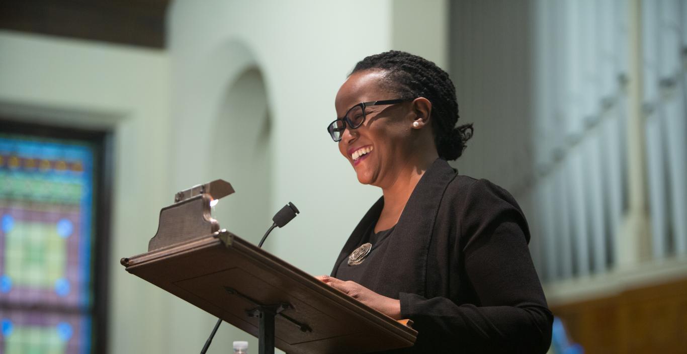 Woman standing at podium talking into microphone with a big smile on her face