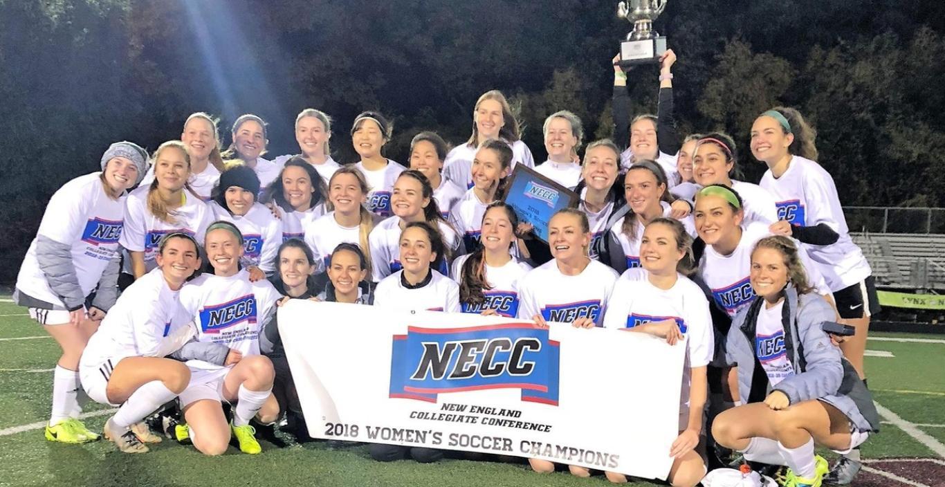 The women's soccer team holding the championship banner on the field. 