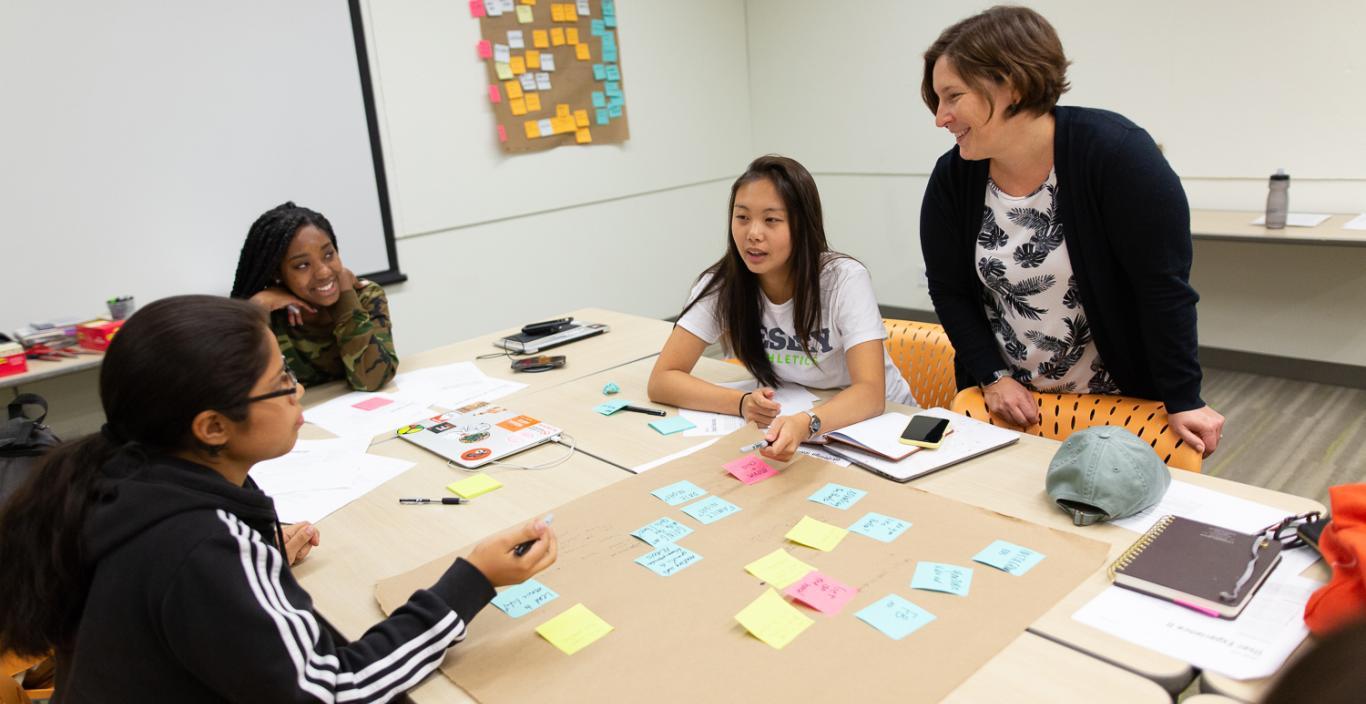 Students and a teacher sit around a table working on a project.