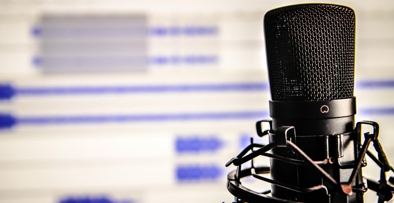 A microphone is in the foreground and a screen in the background.