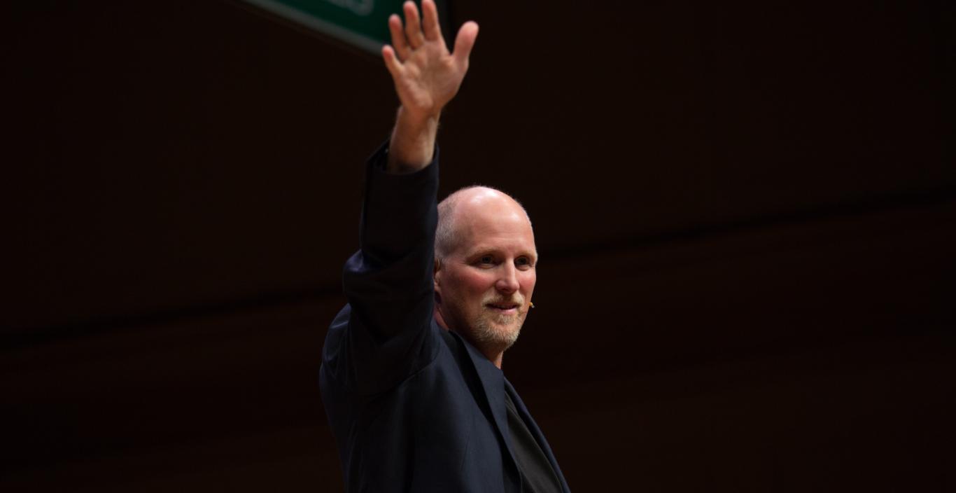 Paul Nicklen on stage, holding one hand up.