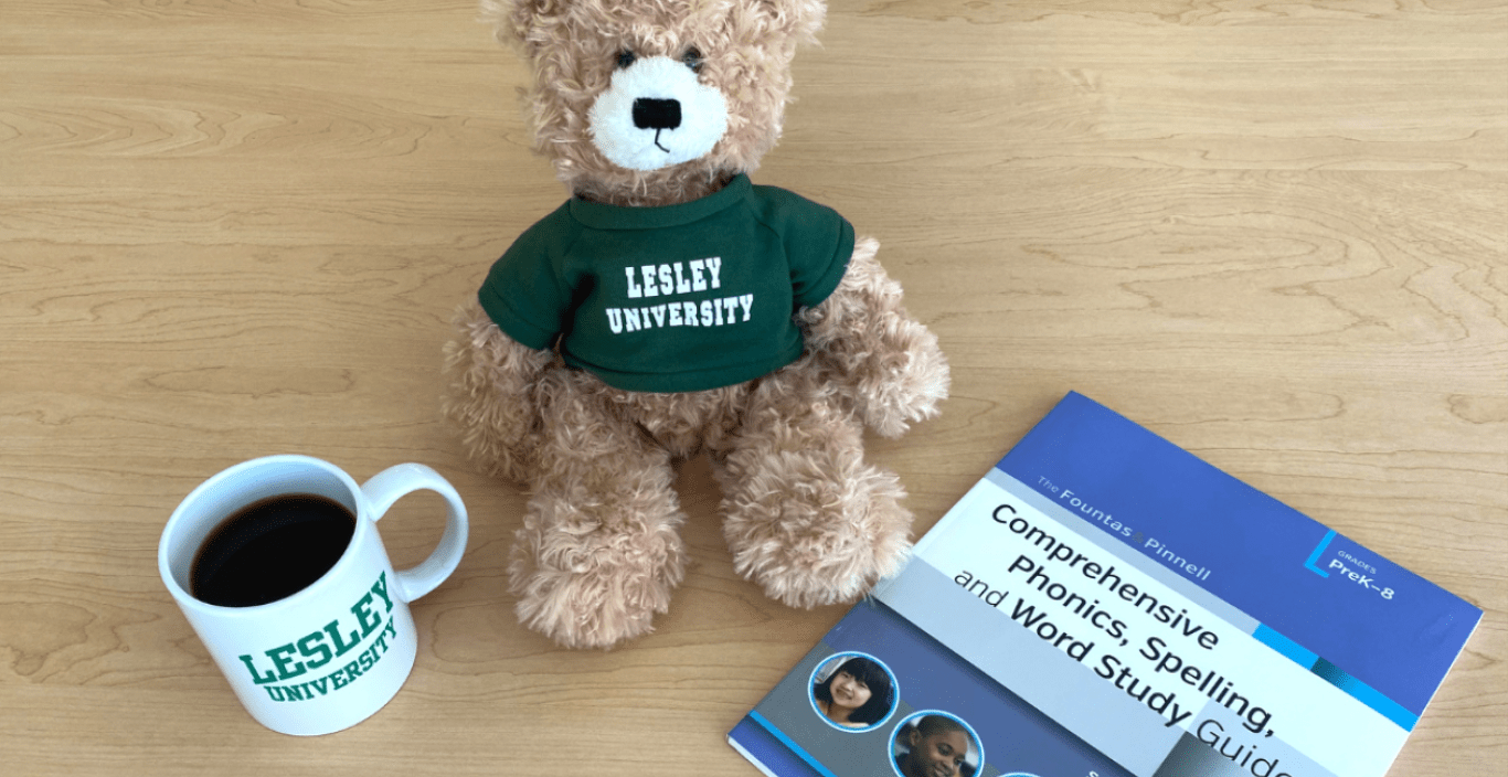 A photo of a Lesley mug filled with coffee, a teddy bear wearing a green Lesley t-shirt, and a book. 