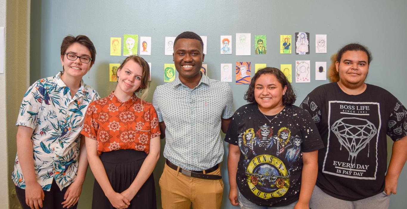 Rocky Cotard with four high school students from the program, standing in front of art at the final showcase.