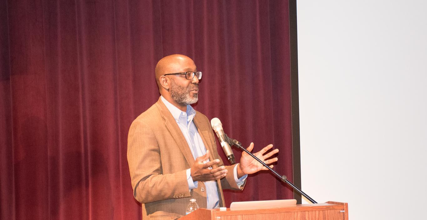 Trent Masiki speaks at a podium on the theater stage.