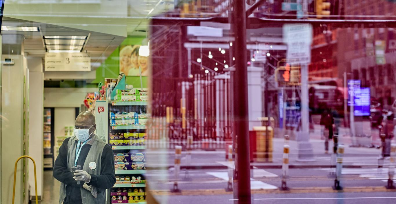 Image of a male Walgreen employee with a mask at work with the reflection of the street in the window