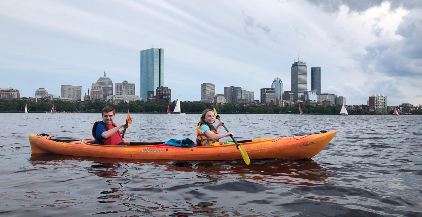 Two people on a kayak on the Charles River with the city in the background