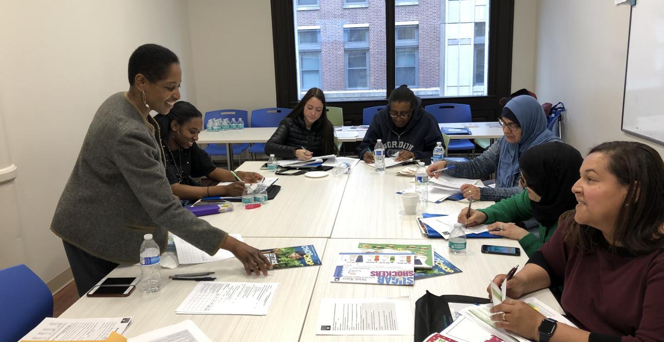 A group of people sit around a table with paper materials on it.
