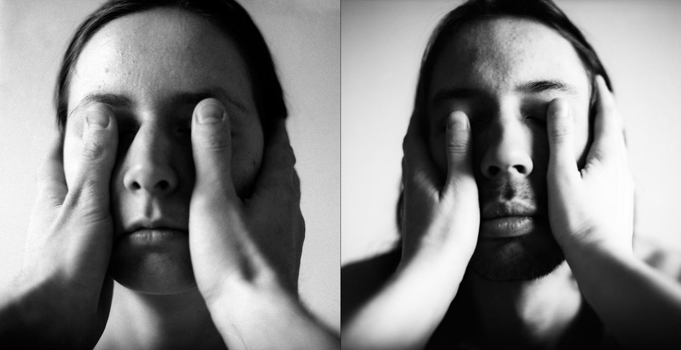 black and white photo of two people standing with another person's thumbs covering their eyes