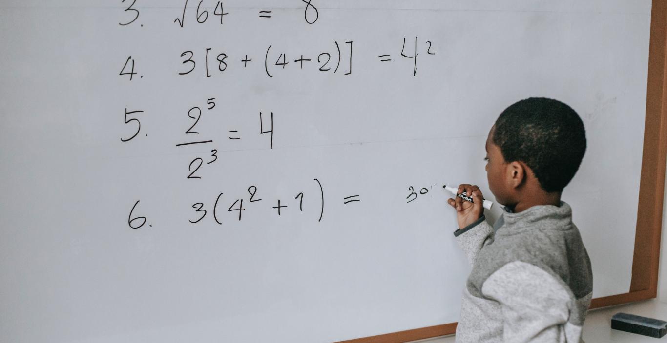 Small Black child doing a math problem at a whiteboard