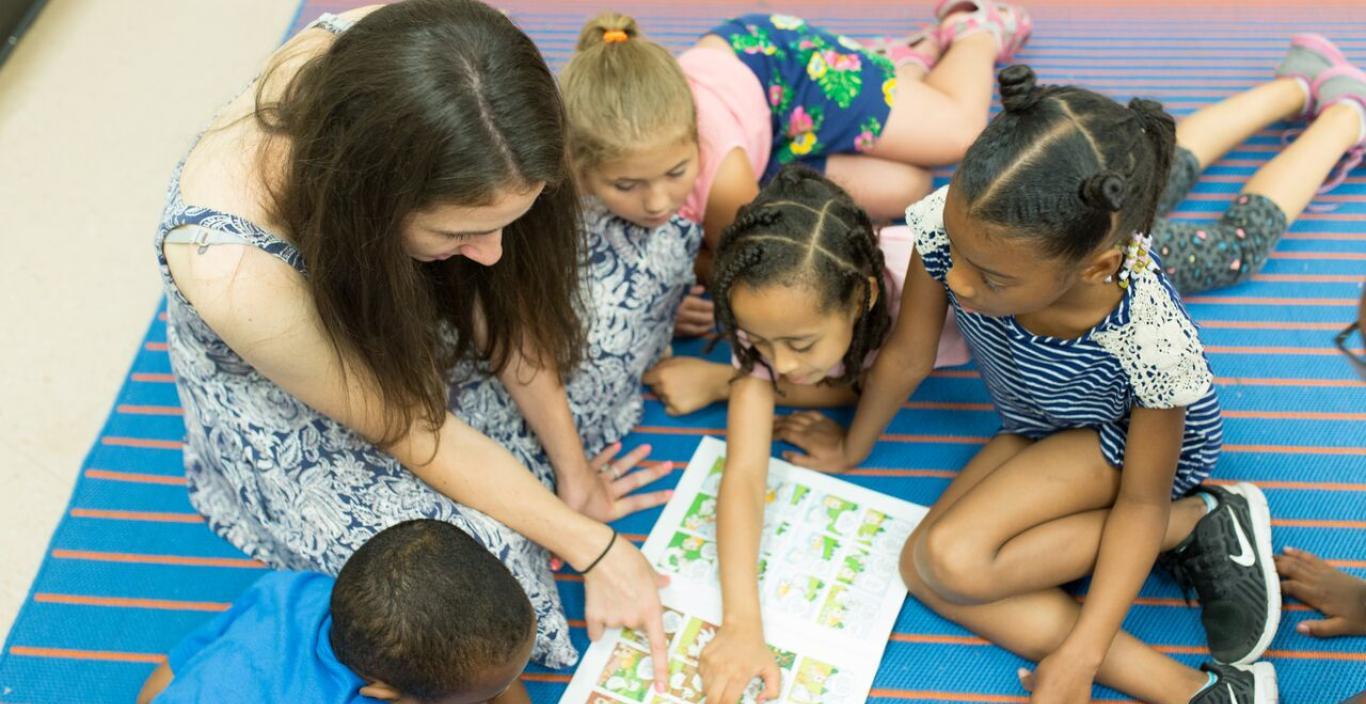 Teacher and students in the classroom, reading a book on the floor 