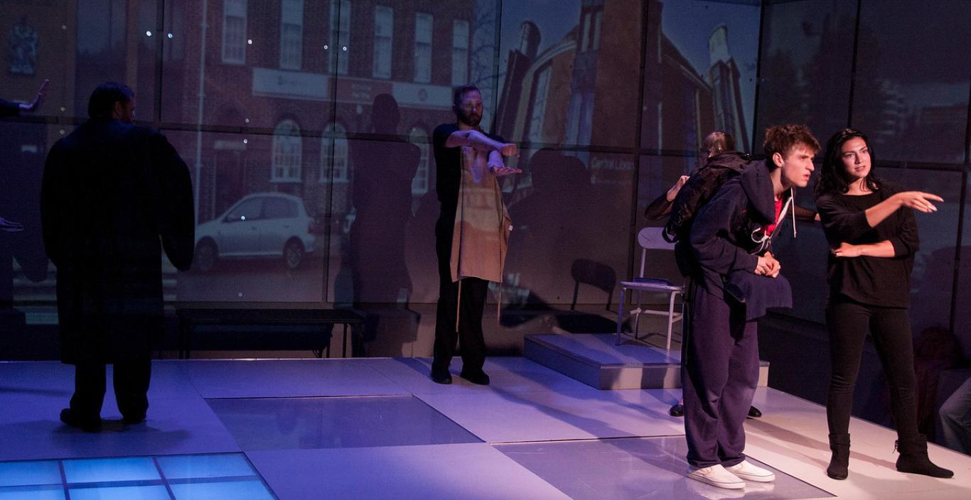 Actors on stage during a performance with dark lights and projections