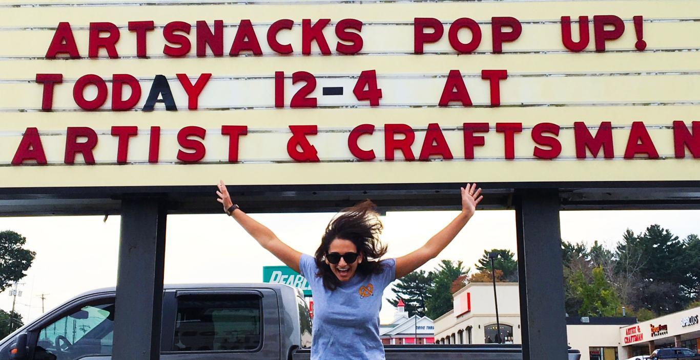 Sarah jumps for joy infront of store sign on side of road