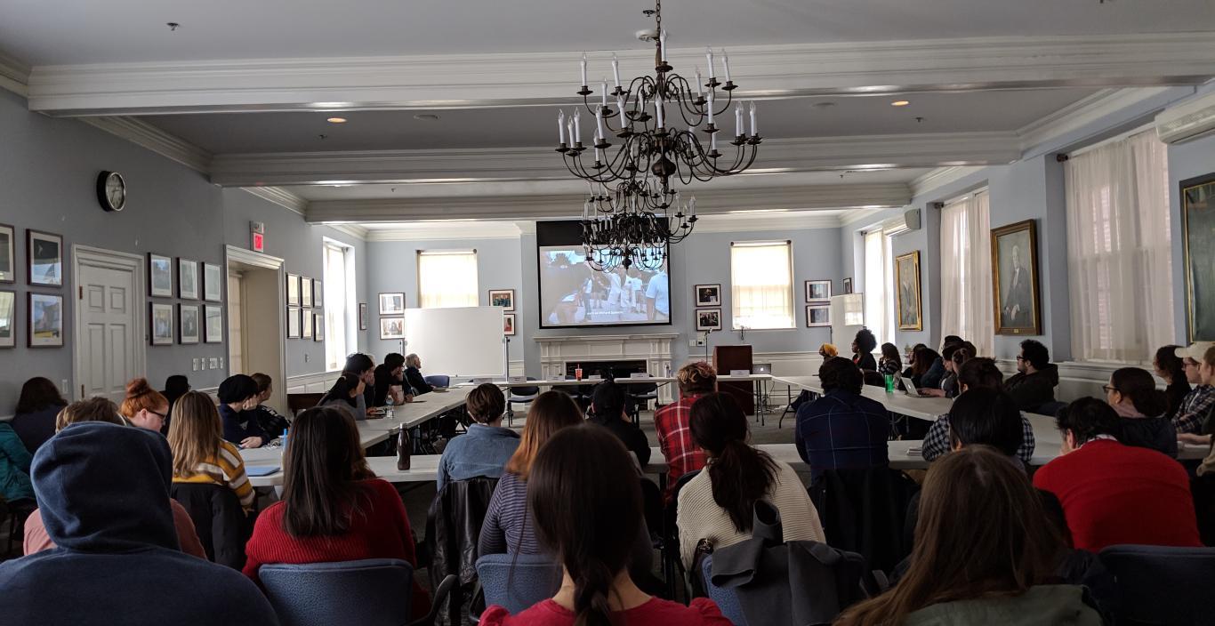 A photo of a large audience in Alumni Hall listening to a panel of speakers during the day.