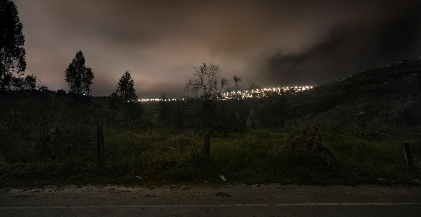 photograph of dark field with city lights in valley below
