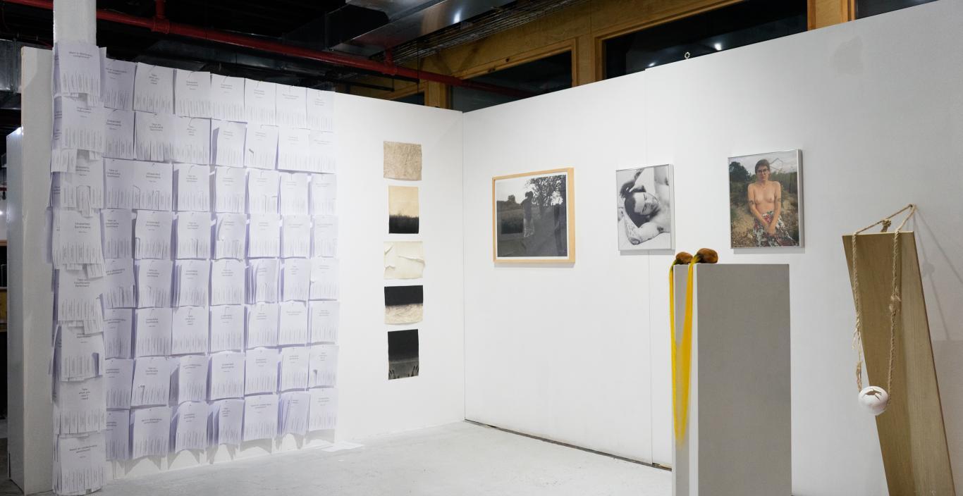 gallery exhibit with papers stuck to the white wall and framed images behind pedestals