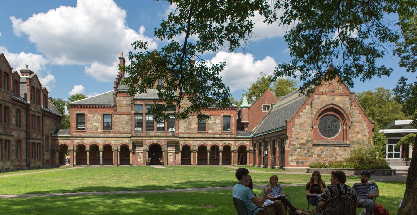 Students sit in chairs in a circle having a class discussion on Lesley's lawn.
