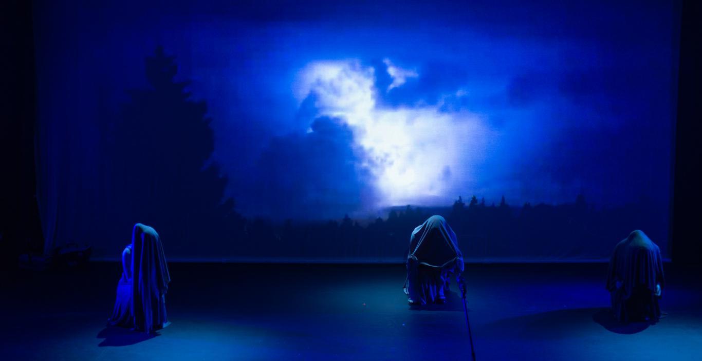 A photograph of the Marran Theater stage during a dress rehearsal of the Oxford Street Players porduction of Macbeth with three witches in front of a screen of blue clouds