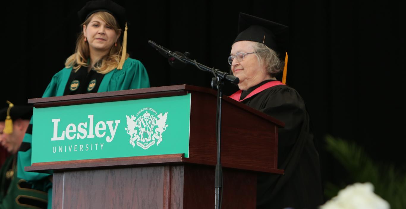 Two women standing on a stage wearing graduation gowns