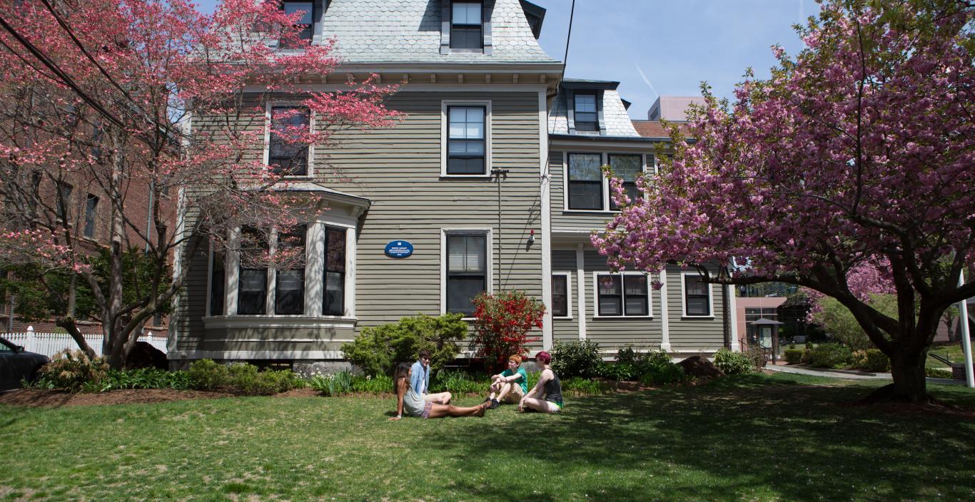 three students sitting on the grass in front of a the president's house