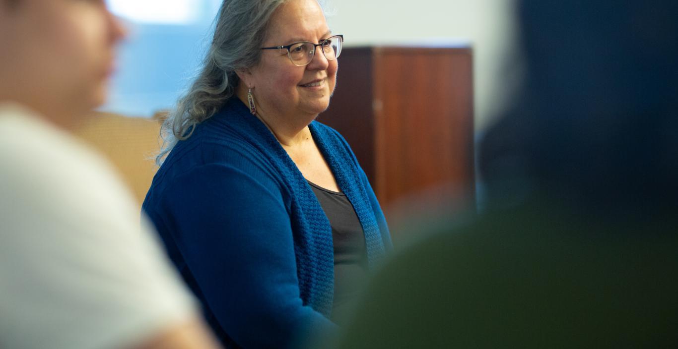 Woman with glasses and a blue sweater seated and speaking to a crowd of students
