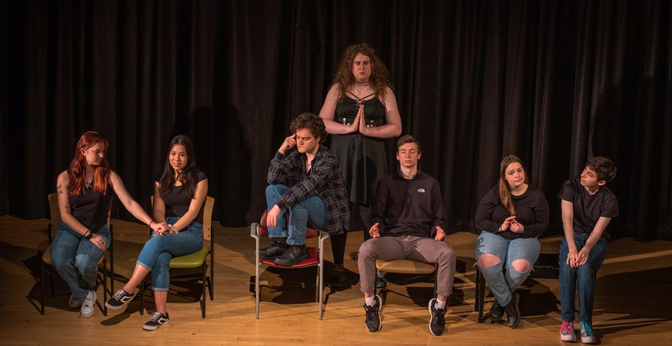 A photograph of a the cast of Small Mouth Sounds seated in a semicircle with one member standing behind on a stage. 