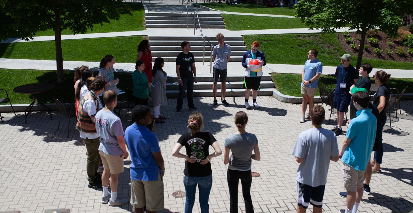 Students standing outside on the quad in a circle on a sunny summer day
