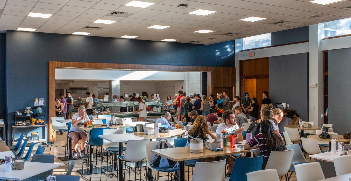 Students in the renovated dining hall sitting in chairs and getting food in a buffet line.