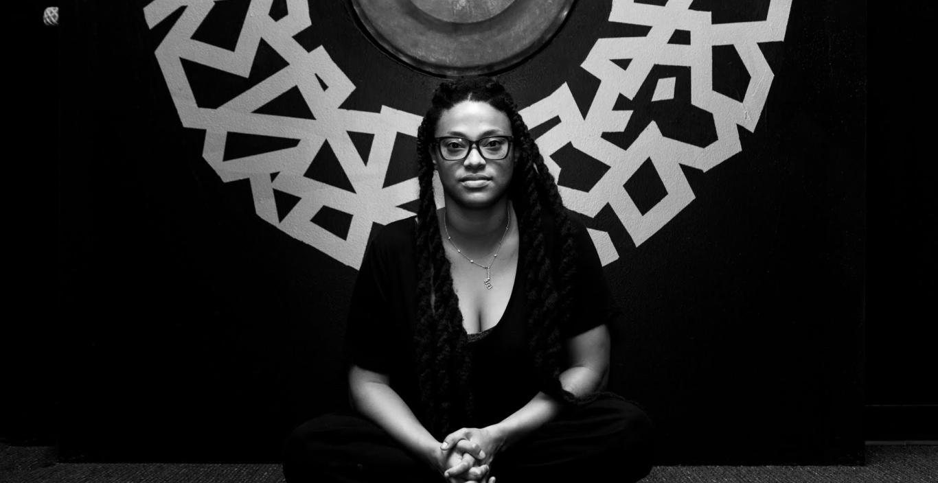 Ya La'Ford sits in front of a mural, photo in black and white.