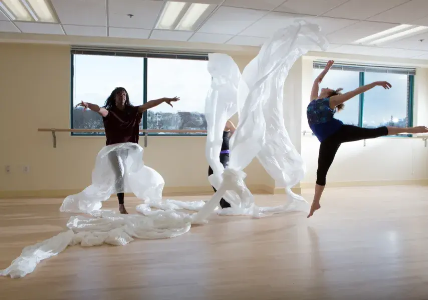 Movement Therapy students, dancing with white sheets in a well-lit dance studio
