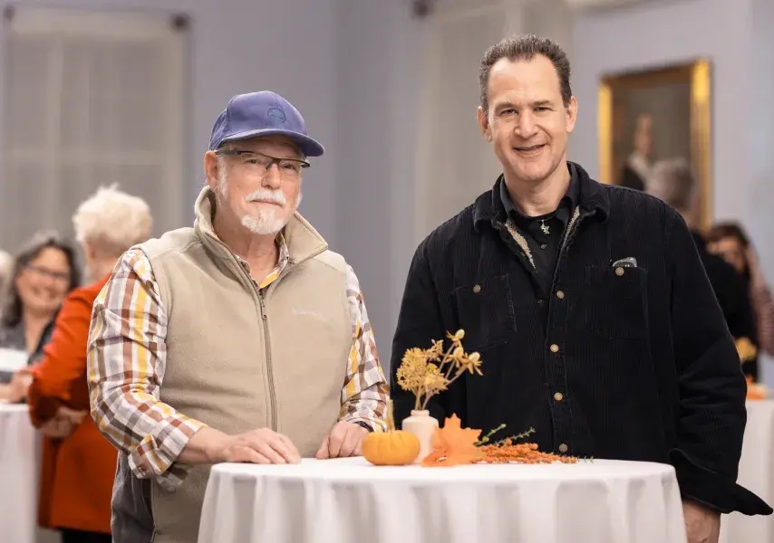 Two people standing side by side at a small round table