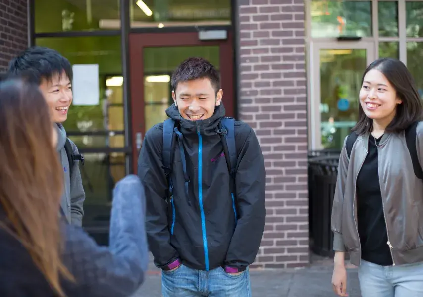 Four students stand outside talking and laughing