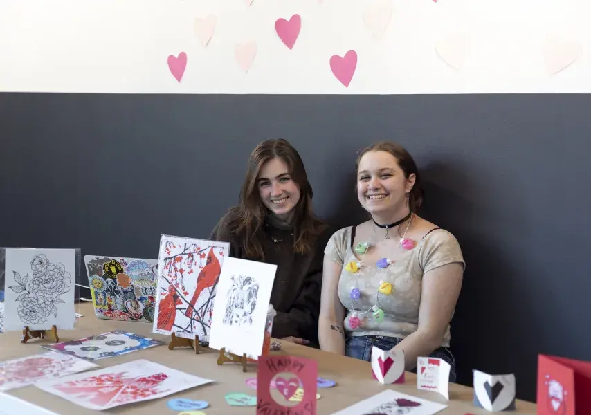 Two students sitting behind a table with displayed artwork