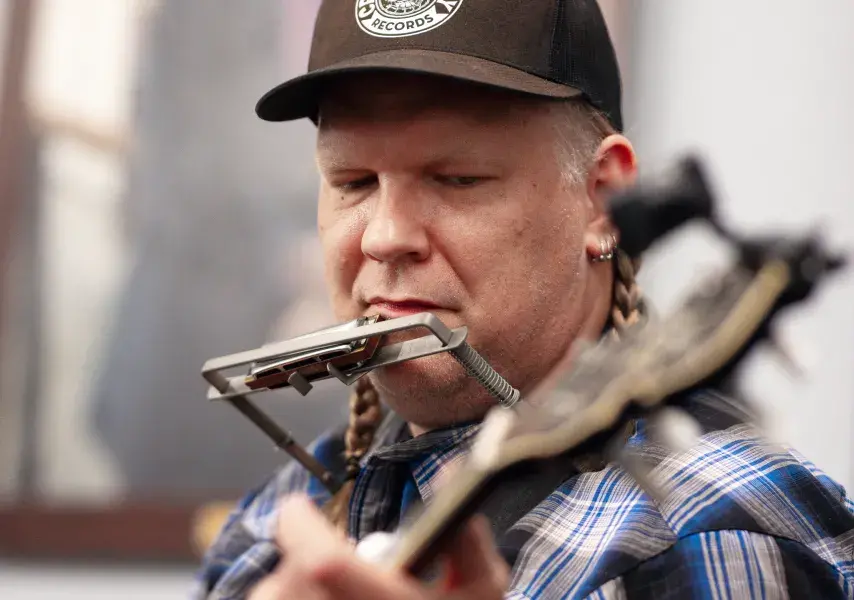 Man wearing a hat playing a guitar attached to a harmonica