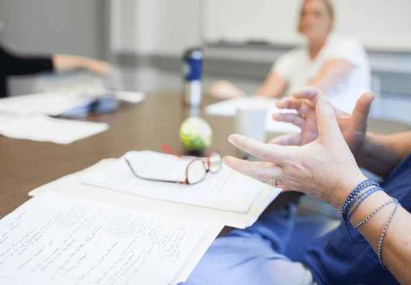 conference table with woman's hands in focus as she explains something to the group