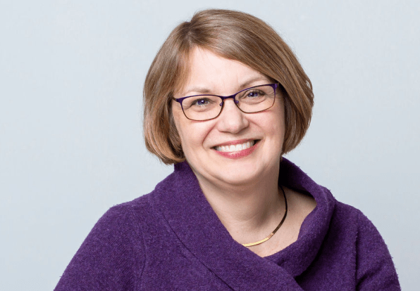 Headshot of Alison Angell. Alison has bobbed blonde hair, glasses, and wears a purple sweater. She smiles while looking at the camera. 