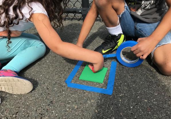 Children on sidewalk using colored tape to make shapes