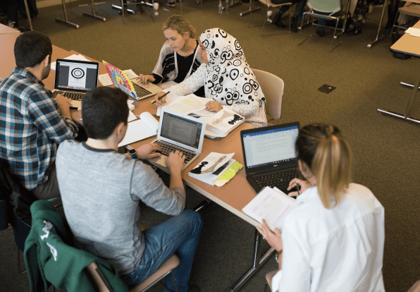 With their laptops and textbooks, a group of 5 students work together at a table.